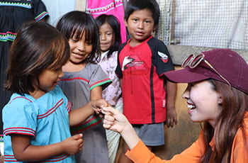 Student knelling in front of a group of children. The student is holding the hand of a little girl. 