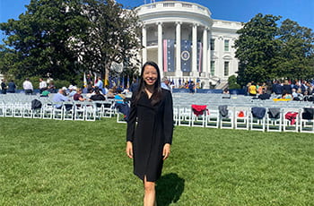 Dr. Jacqueline Burgette standing in front of rows of empty chairs with the White House in the background.