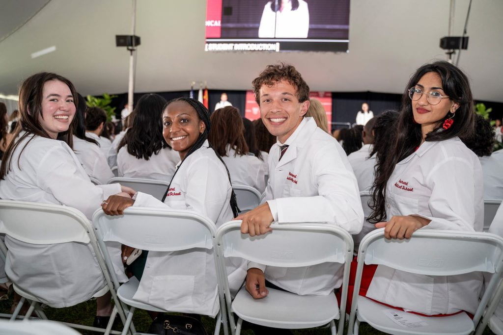 Four DMD students wearing their white coats at the White Coat ceremony turning in their chairs and smiling for the camera.