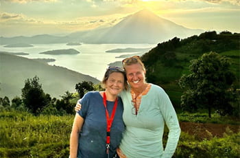 Two instructors pose in front of a lack and a mountain with the sun setting behind it.